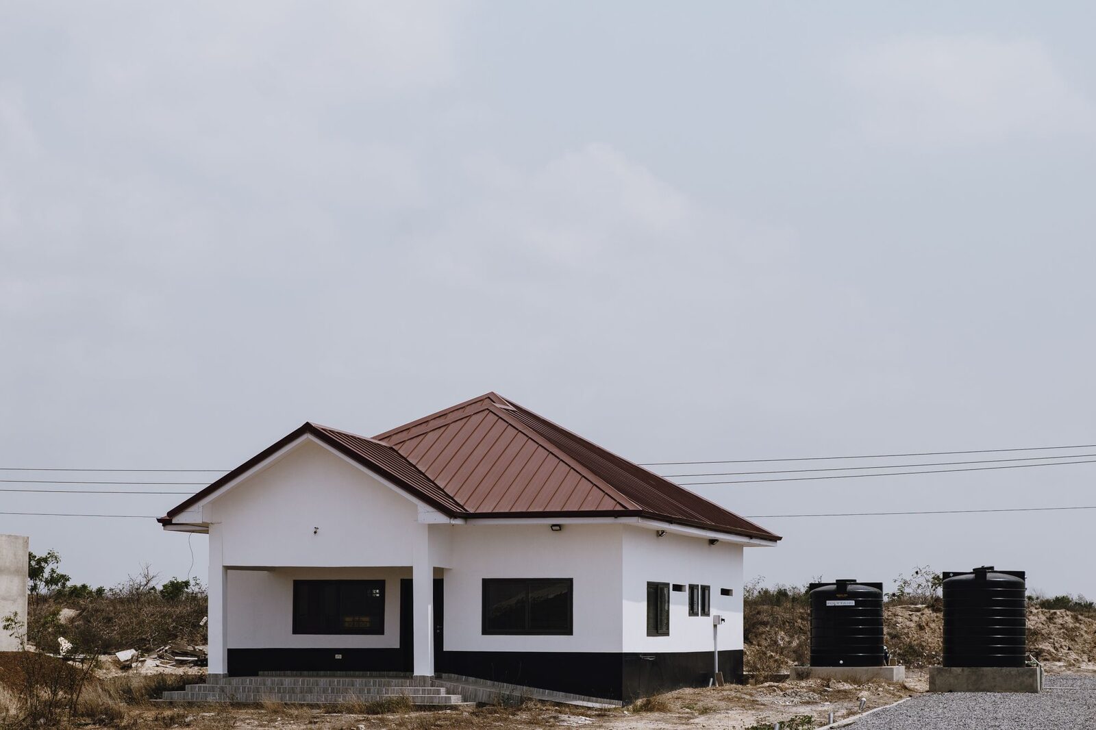 Single-storey house with a red roof and two black water tanks beside it