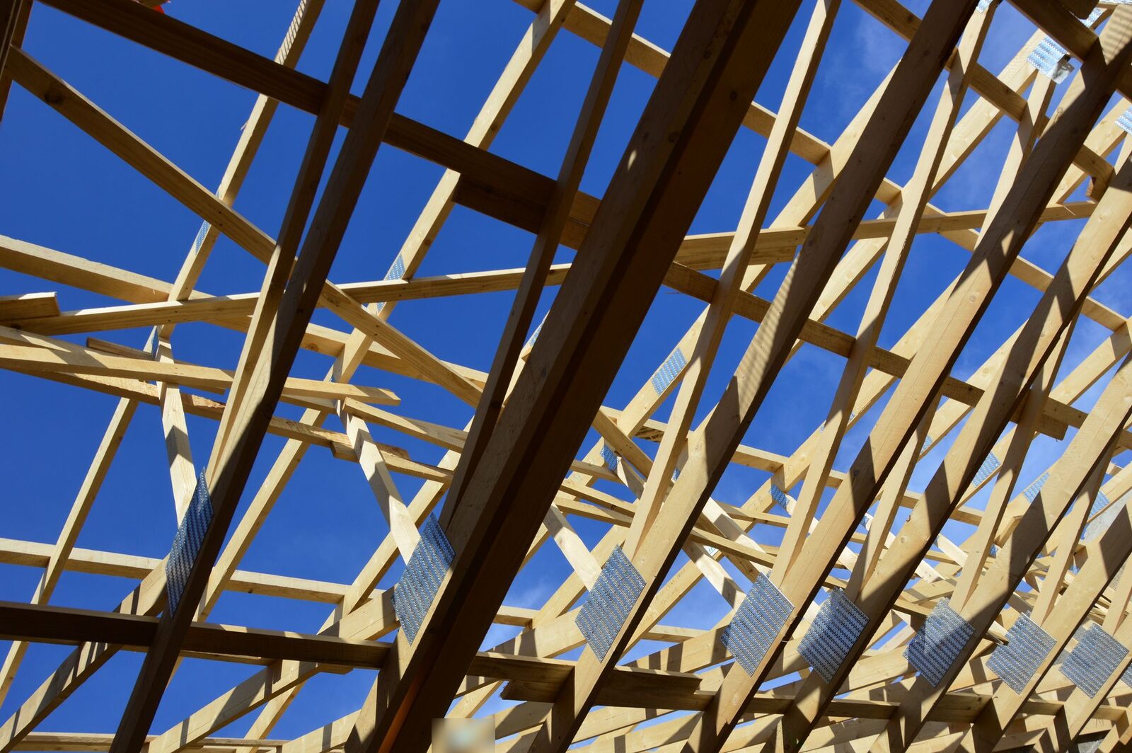 Timber roof trusses joined with metal nail plates, seen from below against a blue sky